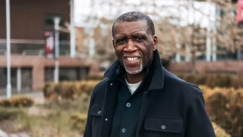PA Media Reverend Clive Foster smiles in a black jacket