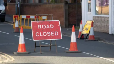 Lincolnshire County Council A sign saying "road closed" in a road, with cones on both sides of it.