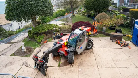 KENT COUNTY COUNCIL A red digging machine works on a set of paving slaps at the top of a steep hill.
