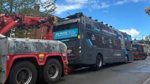 A grey double-decker bus without its roof on the back of a pick-up truck