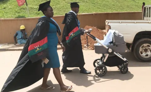 AFP Graduates push a stroller and walk in a campus after the 68th graduation ceremony, where more than 14 000 students received degrees, at Makerere University in Kampala, Uganda, on January 19, 2018