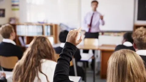 Getty Images Female student raising her hand to ask a question in a classroom