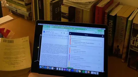 Grace Murray A computer screen open, with words on it, in a room with books all around it. 