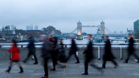 Blurred images of workers crossing London Bridge, with Tower Bridge in the background