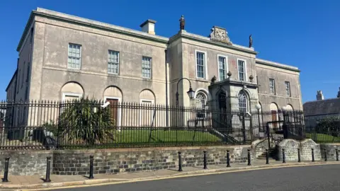 Downpatrick Crown Court. It is grey stone and surrounded by black metal gates. 