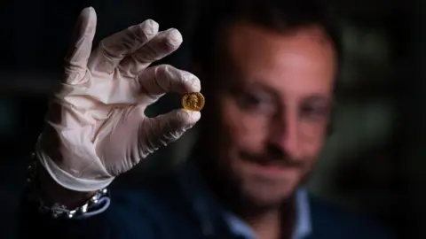 Tony Jolliffe/BBC Alessandro Russo, archaeologist, and gold coin found with the female skeleton