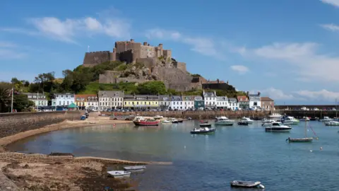 Getty Images Mont Orgueil Castle with buildings and boats in front and blue skies and sea