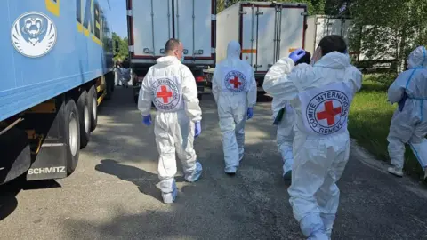 Red Cross members in protective suits walk towards refrigerator lorries with the bodies of killed Ukrainian soldiers. Photo: 16 June 2025
