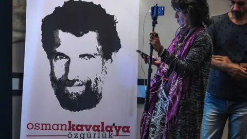 AFP A journalist stands in front of a poster featuring jailed businessman and philanthropist Osman Kavala in October 2018