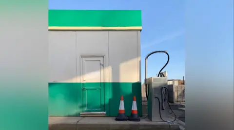 Tom Hicks A green and grey striped building has two cones in front of it.