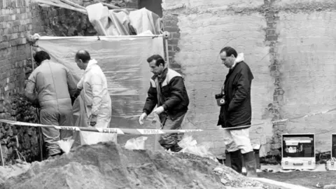 Getty Images Photograph of the garden where Karen Price's body was found at Fitzhamon Embankment in 1989. Four male officers are captured walking into a polyester tent which enclosed the site of her body. They stand behind police tape, one man on the right has a camera on a lanyard around his neck, while two others on far the left wear boiler suits.