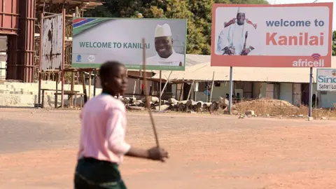 AFP A person walks past boards bearing pictures of Yahya Jammeh in his home town of Kanilai, The Gambia - 22 January 2017