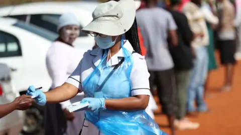 Reuters Someone in PPE going along a queue