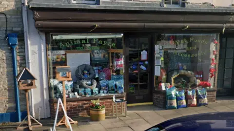 The exterior of a pet shop on a high street. Outside the shop is pet food as well as bird feeders.