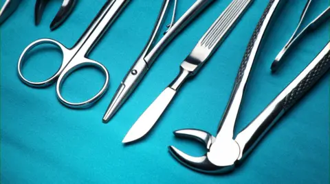 Stock photo shows a range of surgery instruments including scissors laid out on blue cloth