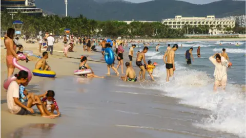 Getty Images People enjoying the beach in Sanya in China's southern Hainan province.
