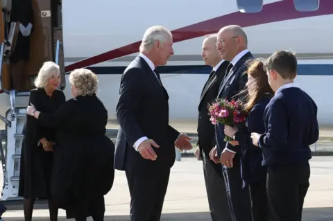 PA Media King Charles and Camilla are greeted at Belfast City Airport by Lord Lieutenant of Belfast Fionnuala Jay-O'Boyle, Northern Ireland Secretary Chris Heaton-Harris, airport chief executive Matthew Hall and schoolchildren Ella Smith and Lucas Watt