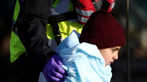 Reuters A migrant child is escorted by Border Force staff into Dover harbour after crossing the channel last week.