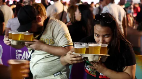 Reuters A woman holding four plastic cups of beer and sipping from one