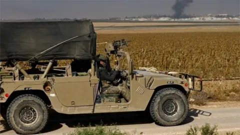 Reuters Israeli soldier uses phone while smoke rises over Gaza in distance