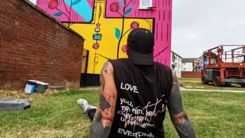 Andy Dice Davies Artist looking up at street art on the side of a house