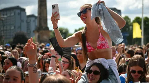 Getty Images Fans partying in the sun at a music festival, including one woman sitting on the shoulders of her friend