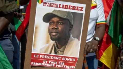 AFP This photograph taken on August 19, 2023 at Place de la Republique in Paris shows supporters of the detained Senegalese opposition leader Ousmane Sonko holding a placard demanding his release.