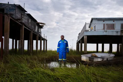 Jasper Doest man stood between 2 homes on stilts. One higher up than the other