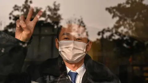 Getty Images A hotel guard gestures while looking at the camera in Wuhan in China's central Hubei province