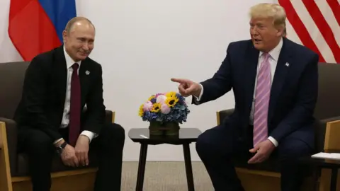 Mikhail Svetlov/Getty Images Vladimir Putin and Donald Trump sitting together in 2019. Their country's flags are draped behind them, and Trump is gesturing with his hand while Putin smiles.