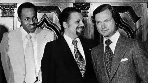 AFP via Getty Images A black and white photo shows Buhari wearing a suit and tie and standing besides King Gustaf and Sheikh Yamani