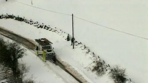 Aerial shot of a white Land Rover on a country road, surrounded by deep snow.