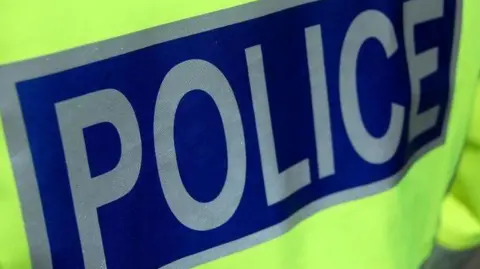 BBC A close up of the back of a police officer's high visibility jacket. The word "police" is in silver letters on a dark blue background.