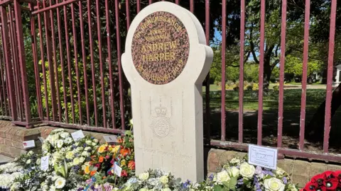 A stone memorial in Andrew Harper's name, surrounded by floral tributes.
