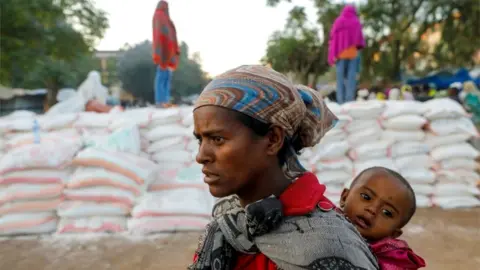 A woman carries an infant as she queues in line for food, at the Tsehaye primary school, in Shire, Tigray region, Ethiopia