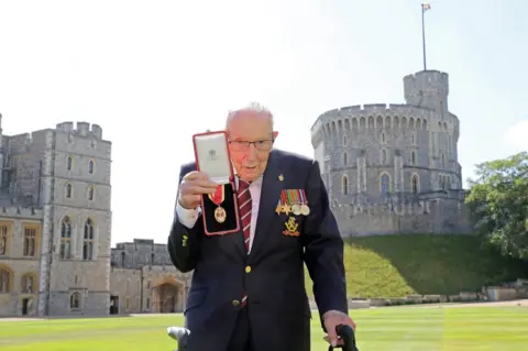 Getty Images Captain Sir Tom Moore holds out his medal with Windsor Castle behind him