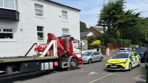Reach PLC Street with car carrier truck and police car outside opening of white building