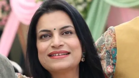 Gauri Chaudhary Gauri Chaudhary smiles at the camera. She has black hair and brown eyes and is wearing gold earrings with green and red stones. 