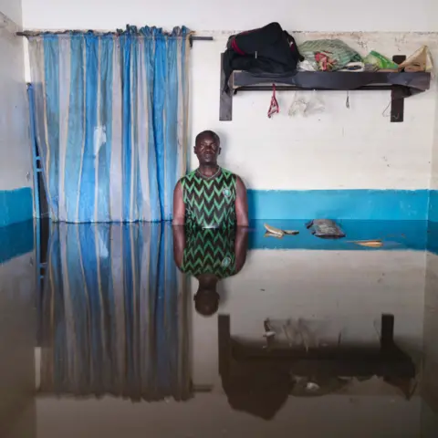 Gideon Mendel Prince Ogiasa Lume standing in flood water in his home in Ogbia Municipality, Bayelsa State, Nigeria - November 2022