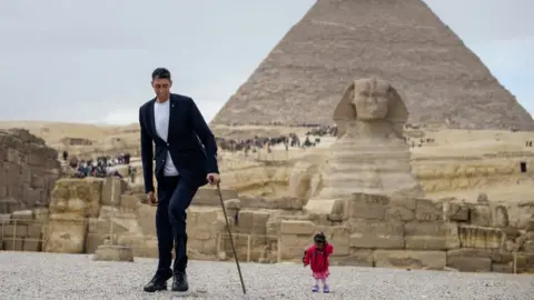 AFP India's Jyoti Amge (R), the world's shortest woman poses for a picture with Sultan Kosen of Turkey, the world's tallest man, at the site of the Pyramids of Giza in Egypt on January 26, 2018, with the Sphinx and the Pyramid of Khafre (also known as Chephren) seen in the background