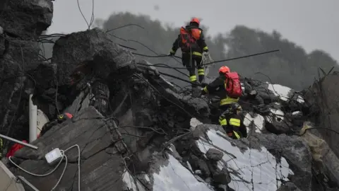 EPA Rescuers climb on foot over large pieces of road wreckage, amid rain and poor conditions