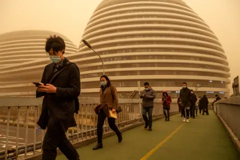 Getty Images People wear protective masks as they walk during a sandstorm on 15 March 2021 in Beijing