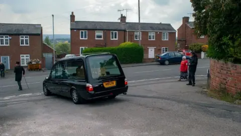 Bella Milroy Hearse carries coffin as people watch