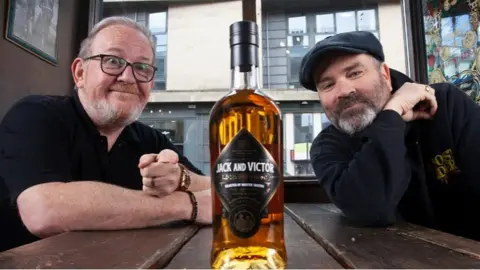 Jack & Victor Greg Hemphill and Ford Kiernan with a bottle of Jack and Victor