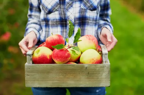 Getty Images A woman holds a crate of apples