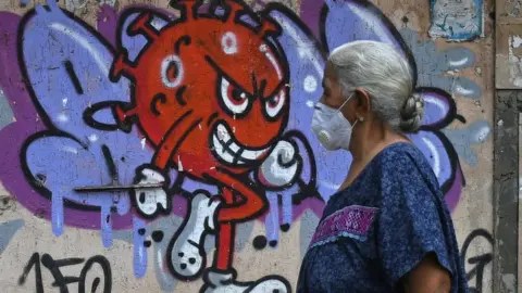 Getty Images A woman wearing a protective mask walks past a graffiti painted to create awareness about the coronavirus disease in Mumbai. 12 Oct 2021