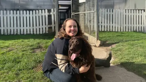 Andrea Burley Andrea Burley and her dog Baxter in front of the kennel