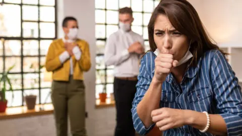 Getty Images A woman coughs in work