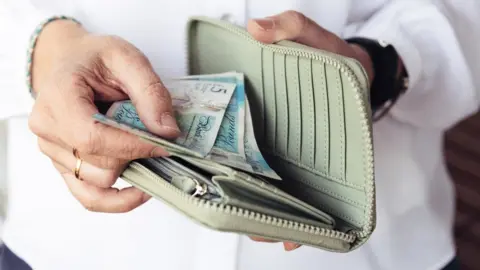 Getty Images Woman looking at money in her purse