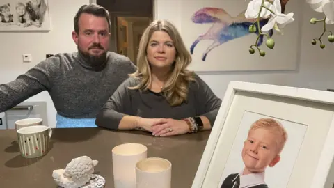 Sam Read/BBC Matt and Louise Fox sat next to each other with a framed photo of their son George in front of them